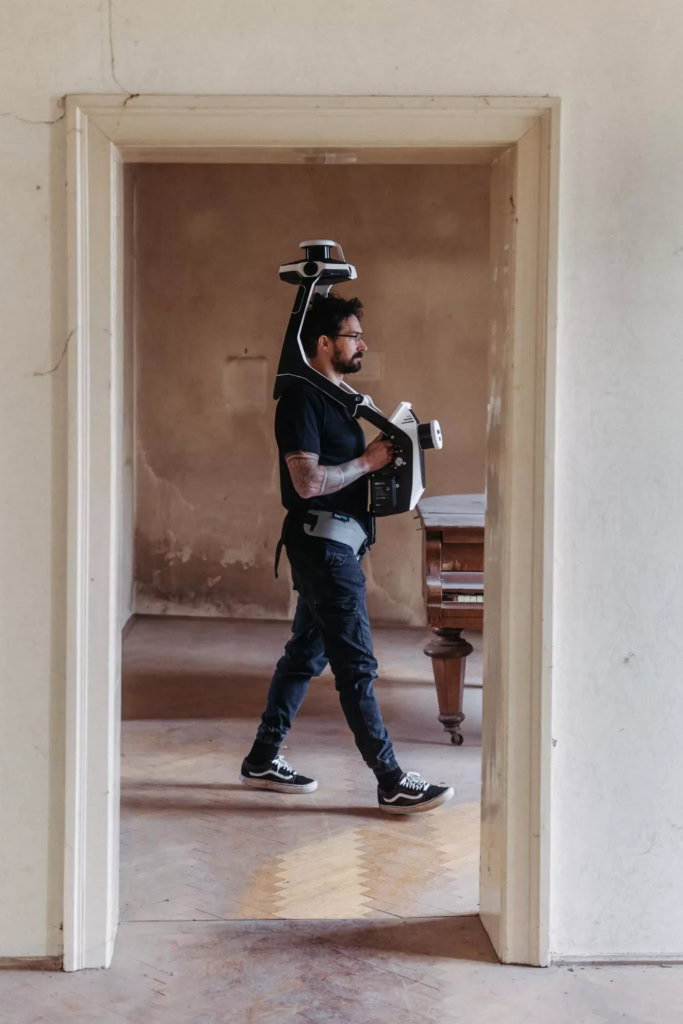 Ein Mann geht mit einem 3D-Laserscanner durch eine offene Tür.