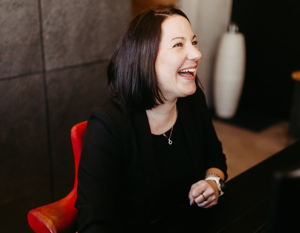 Eine Frau sitzt an einem Schreibtisch und lacht.