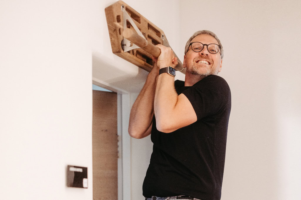 Ein Mann hält eine hölzerne Klimmzugstange.