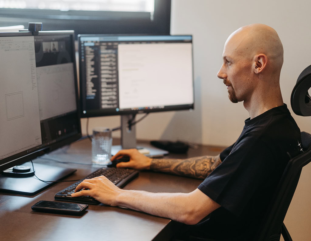 Ein Mann sitzt an einem Schreibtisch mit zwei Computermonitoren.