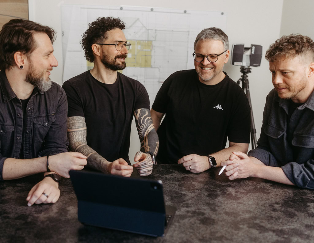 Vier Männer sitzen an einem Tisch mit einem Laptop.