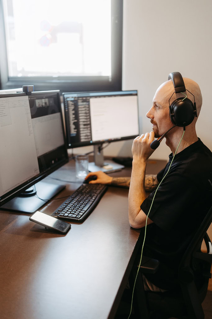 Ein Mann mit Kopfhörern sitzt an einem Schreibtisch mit zwei Computermonitoren.