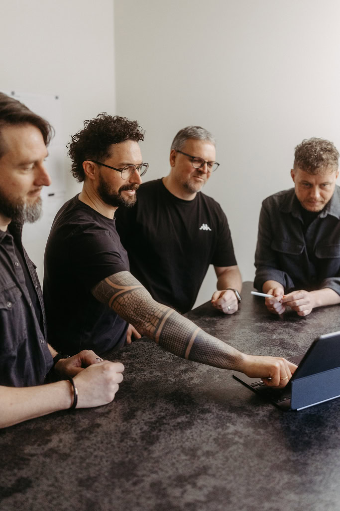 Vier Männer sitzen an einem Tisch mit einem Laptop.