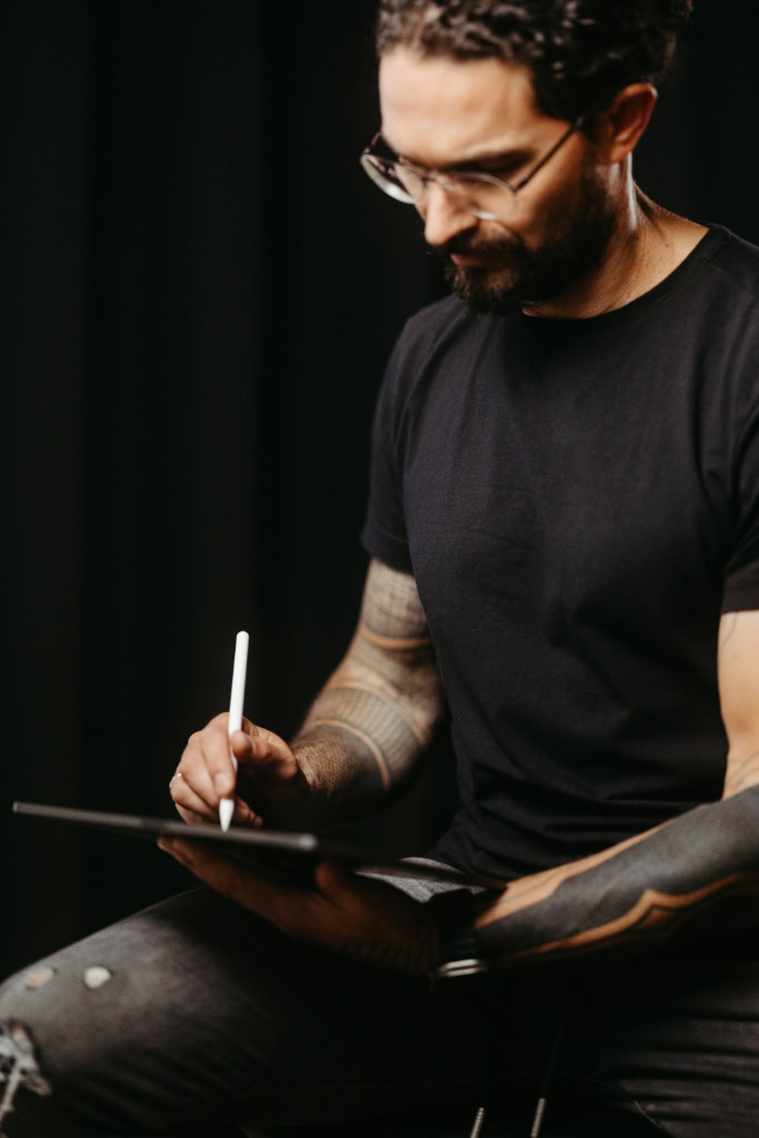 Ein Mann mit einer Tätowierung am Arm schreibt auf einem iPad.