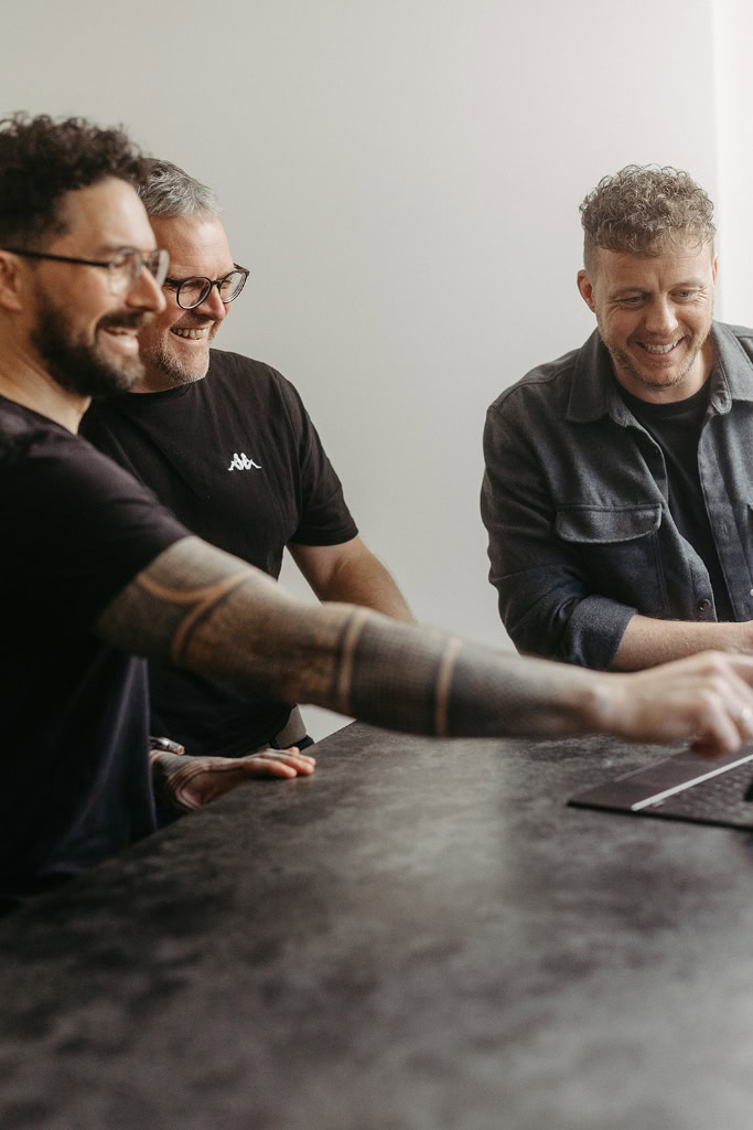 Drei Männer sitzen an einem Tisch mit einem Laptop.