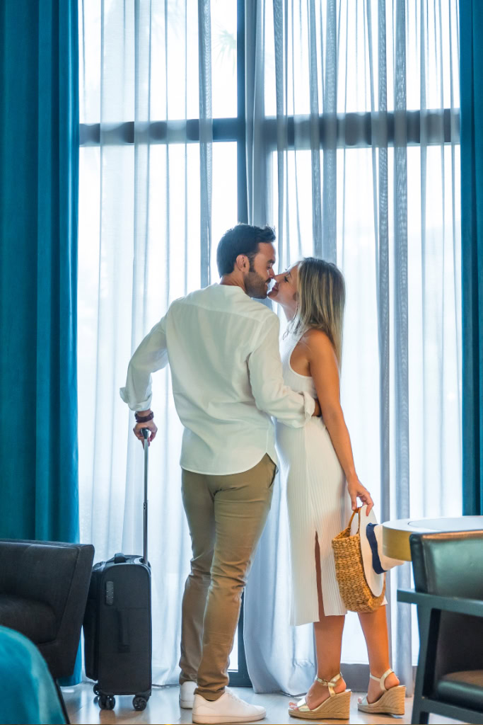 Ein Paar küsst sich vor einem Fenster in einem Hotelzimmer.