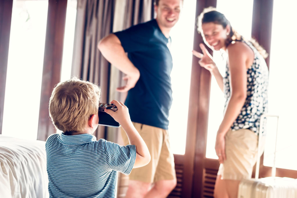 Ein Junge fotografiert einen Mann & eine Frau in einem Hotelzimmer.